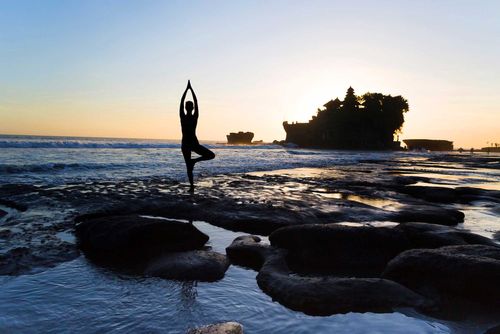 Vrikshasana tree pose from yoga by woman silhouette on sunset near Tanah lot temple