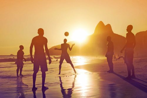 Silhouette of locals playing ball game at sunset in Ipanema beach, Rio de Janeiro, Brazil.